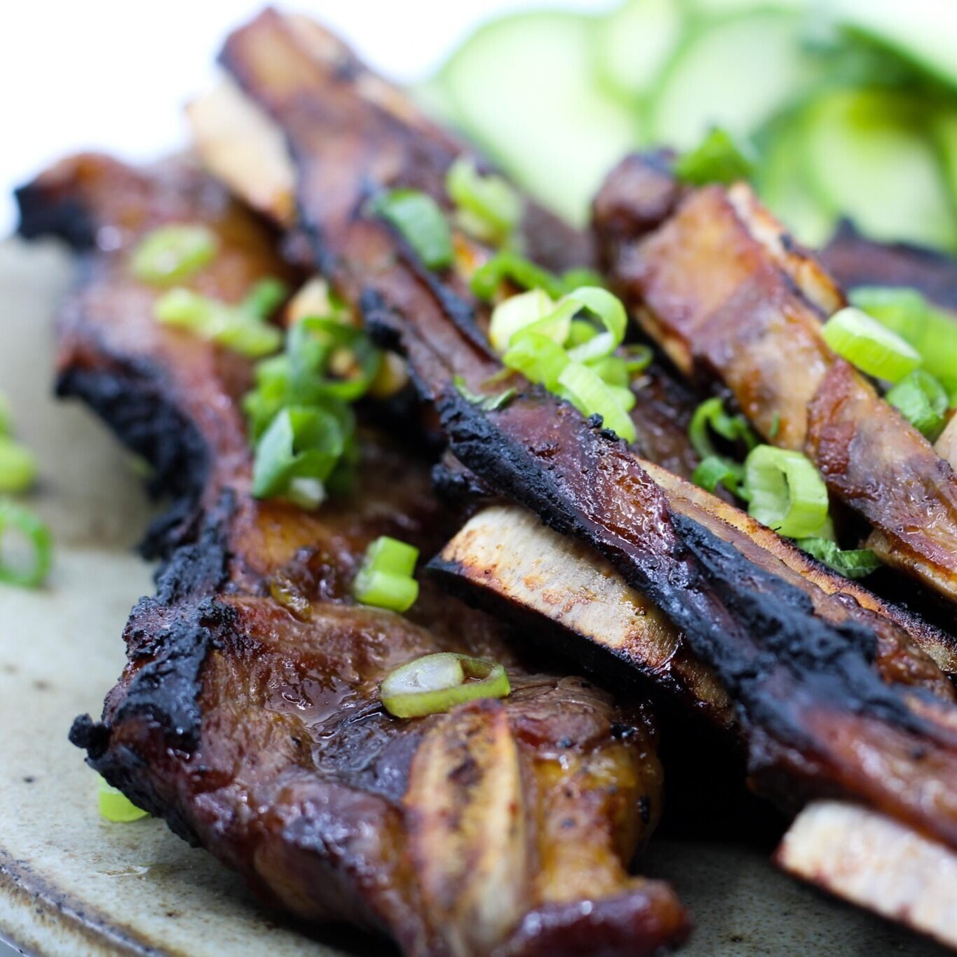 Grilled pork ribs garnished with chopped green onions, served on a plate with fresh cucumber slices.